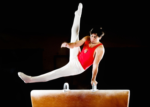 Young muscular man doing gymnastic exercises on pommel horse.   