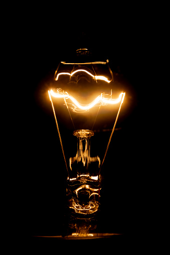 Close up of a vintage light bulb with glowing filament isolated on black background