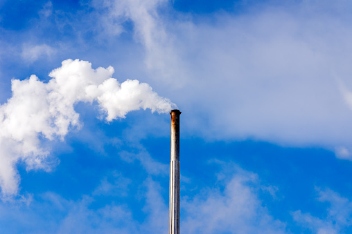 One Industrial smoke pipe from chimney on blue cloudy sky.White smoke emanates from the pipe.