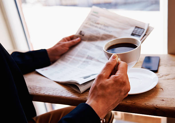 Close up white coffee cup on yellow table at sunrise sand beach with newspaper in the morning , Thailand