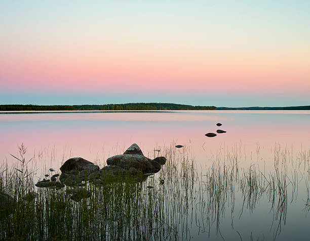 Sunset in Hankasalmi, Finland, at the shore of Lake Kuuhankavesi. Some stones are seen in the water.