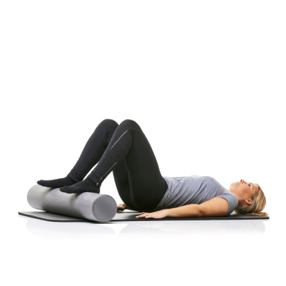 A young woman lying on an exercise mat with her feet on a foam roller