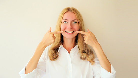 Portrait of happy smiling young woman points with fingers to her white clean teeth at home