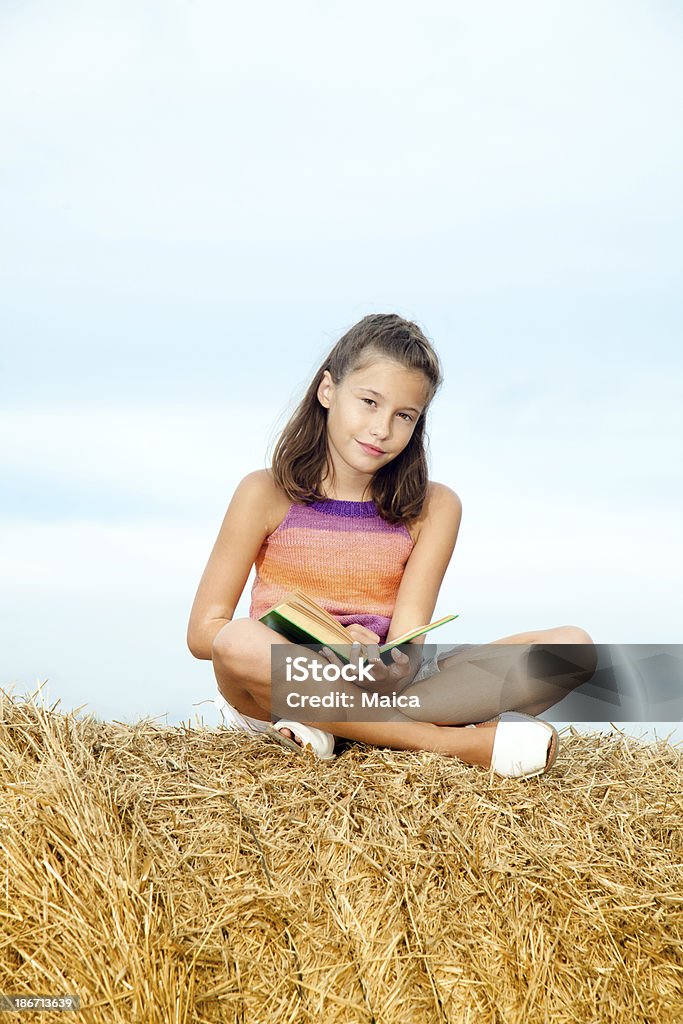 Petite fille assise sur le foin, lecture - Photo de 10-11 ans libre de droits