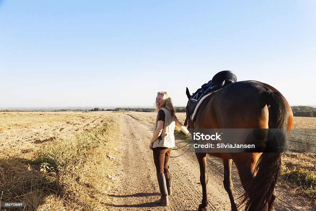 mature woman with her horse walking on rural path mature woman walking with her horse on a rural path near an empty field in autumn, turning her head and smiling 40-44 Years Stock Photo