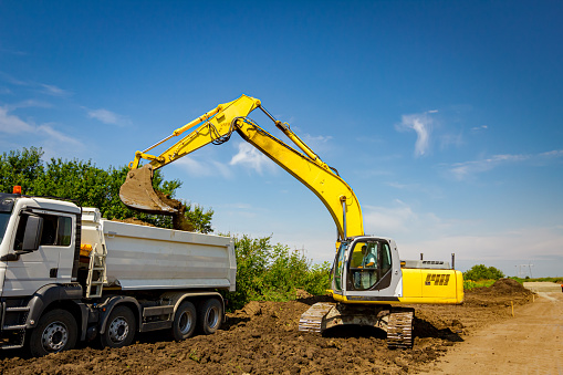 Zrenjanin, Vojvodina, Serbia - July 7, 2019: Caterpillar excavator is filling dumper truck with front bucket full of soil, transportation at construction site.