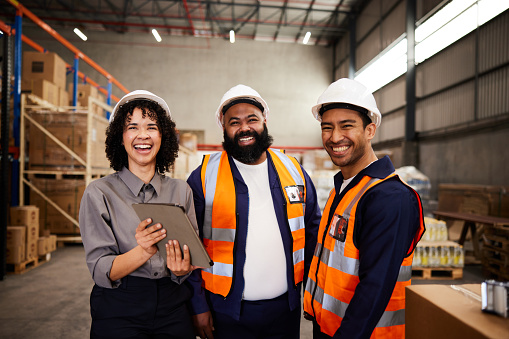 Portrait of a group of workers laughing while tracking shipments using a digital tablet in a large shipping and distribution warehouse