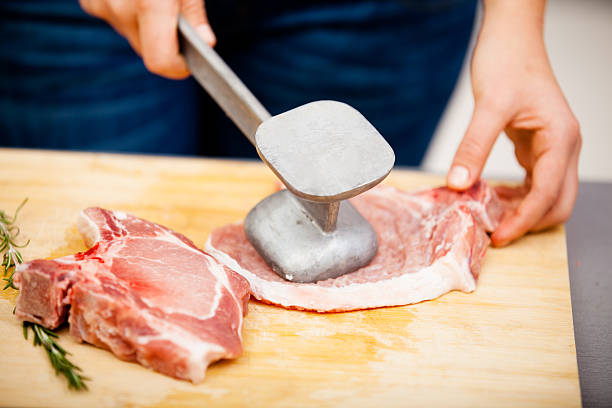 Young woman beating a steak in the kitchen