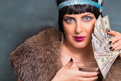 Woman in retro style. fashion of the twenties. Alcohol in a glass. Portrait of an american woman. Dollars and glamor.