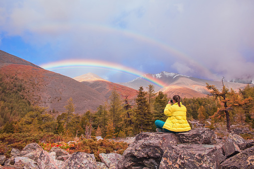 A young girl photographs a rainbow in the mountains.