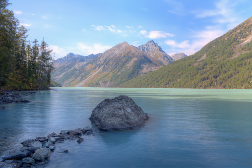 Lake in a mountain valley. Large stone in the lake. Mountainous terrain. Selective focus on stone. Soft focus.