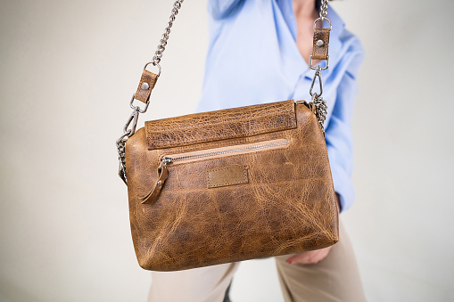 Young unrecognizable Caucasian female fashion model, carrying an brown leather bag