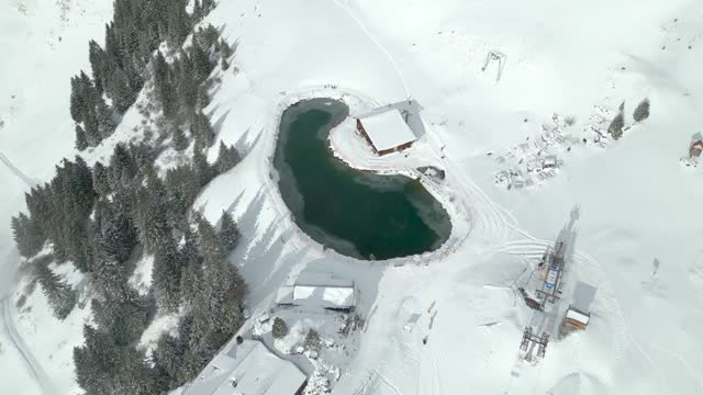 Aerial drone top down shot over partly frozen lake beside chairlift in Engelberg Brunni bahnen, Switzerland on a sunny day.