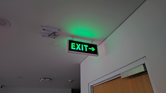 The exit sign hangs above the ceiling, the writing is bright green