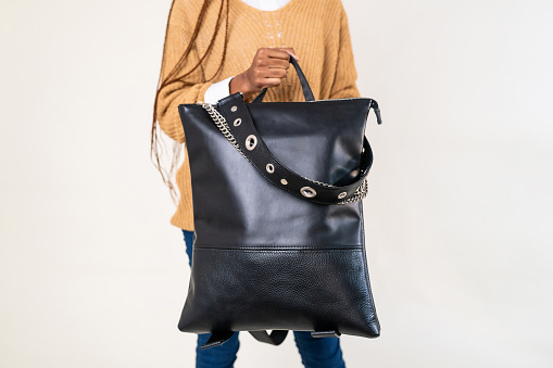 Unrecognizable young female fashion model Black ethnicity, carrying an black leather bag