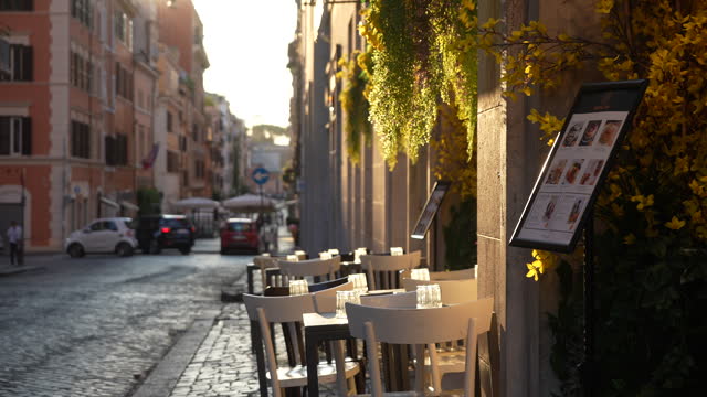 Tracking shot of Italian restaurant table without visitors during sunrise on background of soft sunlight. Empty street cafe. Outdoor cafe in vintage street.