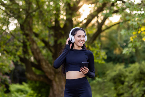 istock Successful slim latin american woman in park during active exercise and jogging uses smartphone app, sportswoman smiling in headphones listening to audio podcasts and online radio 1867245183