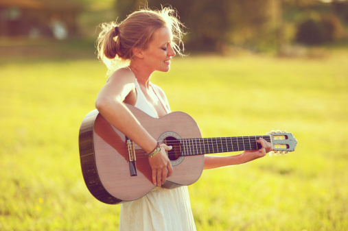 Young woman playing a classic guitar and singing with an emotional expression.