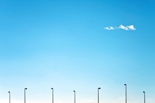 Distant street lamps silhouettes against clear blue sky with single cloud