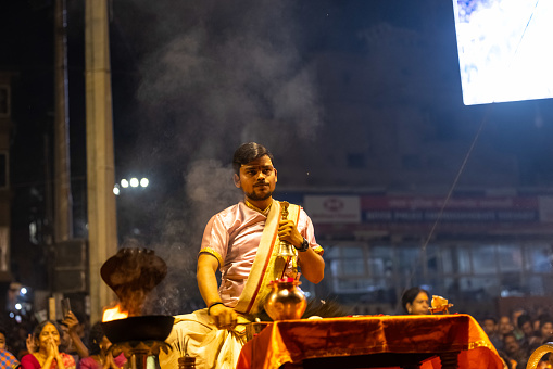 Varanasi, Uttar Pradesh, India - March 2023: Ganga aarti, portrait of hindu male priest performing holy river ganges evening aarti at dashashwamedh ghat in traditional dress with rituals.