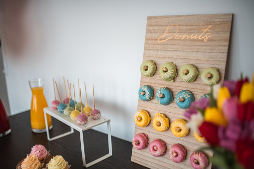 Elegant baby shower centerpiece with a variety of donuts on a bespoke board, cake pops, and a bouquet of tulips adding a fresh accent.