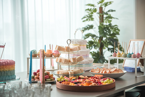 A contemporary baby shower display featuring a colorful cake, assorted snacks, and a drink dispenser, ready for the guests' arrival.