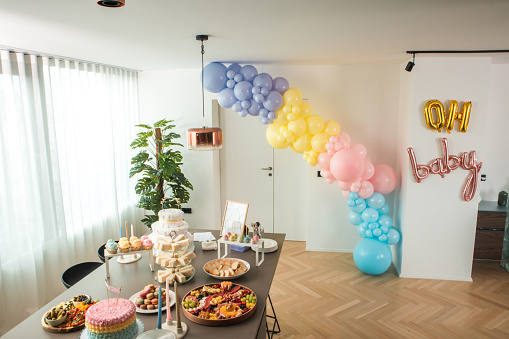 A bright modern setting for a baby shower featuring a sumptuous buffet, a standout cake, and cheerful balloons.