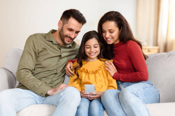 istock Happy Arabic family holding using mobile phone sitting at home 1867282037