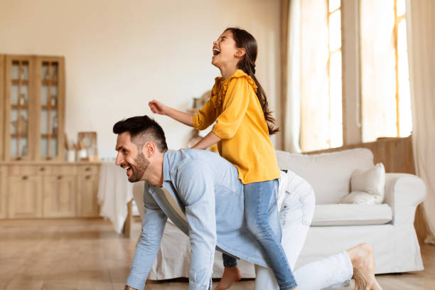 istock Young father riding daughter on back fooling at home 1867283077