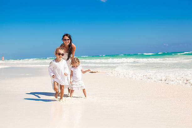 istock Young mother and little daughters walking on tropical white beach 186728657