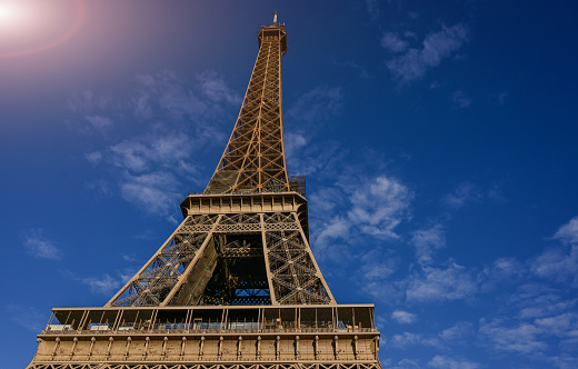 Paris, France, July 1, 2022. Iconic image of the Eiffel Tower seen from below. The warm light of late afternoon illuminates it fully. Blue sky with white clouds.