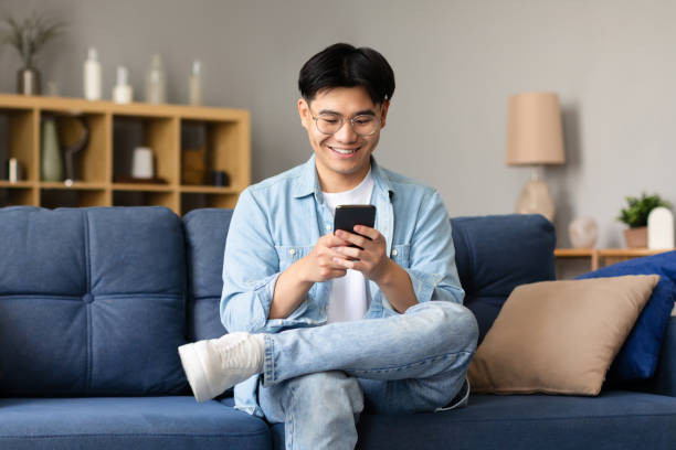 istock Happy Korean Young Man Using Smartphone Texting Sitting At Home 1867300484