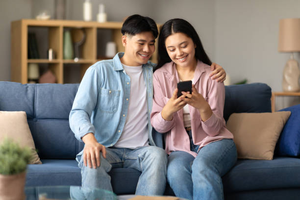 istock Asian couple messaging on cellphone at home interior 1867301035