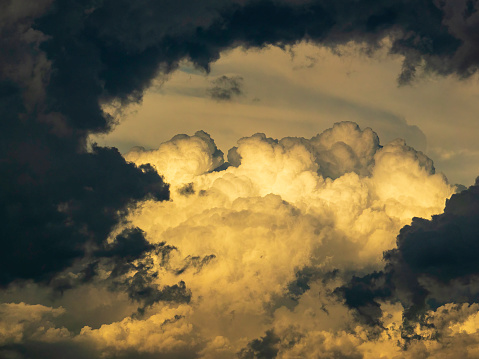 Billowing cumulus clouds in evening sunlight, partly framed with dramatic effect by dark ragged storm clouds in the foreground, at the end of summer in southwest Florida