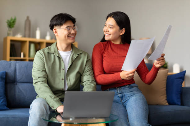 istock Smiling Korean Spouses Using Laptop Holding Bills Papers At Home 1867303730