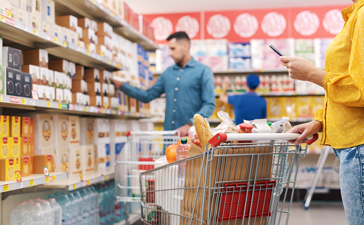 Supermarket interior with shelves: people doing grocery shopping, selective focus