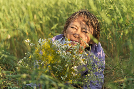 thoughtful, modern retiree immerses herself in the tranquility of a summer meadow, the wildflowers in her hands serving as a poignant reminder of life's continuous journey