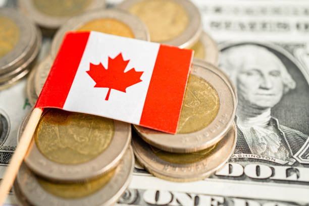 istock Stack of coins with Canada flag and US dollar banknotes. 1867347107