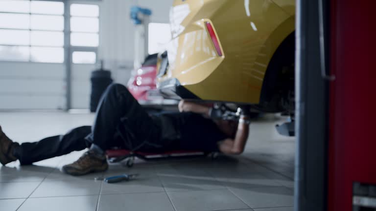 Male mechanic on creeper working under car in auto repair shop