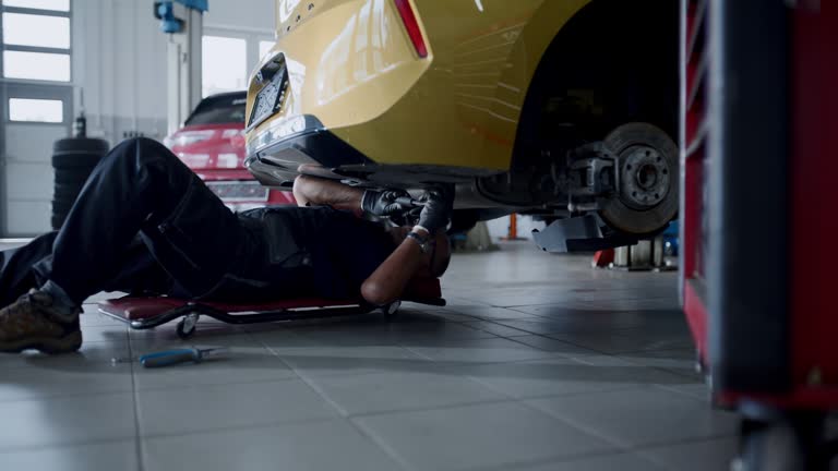 Male mechanic working on creeper under car in auto repair shop