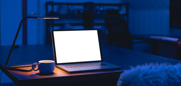 istock Laptop and cup on a table in a dark room with a blank screen at night. 1867370387