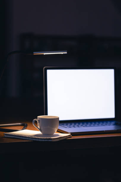 istock Laptop and cup on a table in a dark room with a blank screen at night. 1867370392