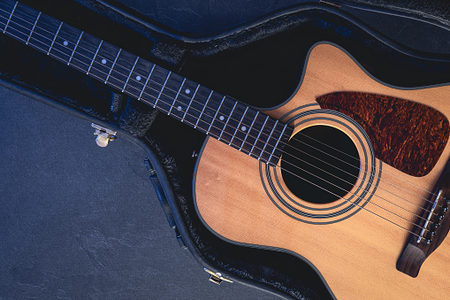 Acoustic guitar in a protective case on a dark background, top view, musical background.