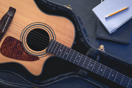 Acoustic guitar in protective case and notepad with pencil, top view, music learning concept.