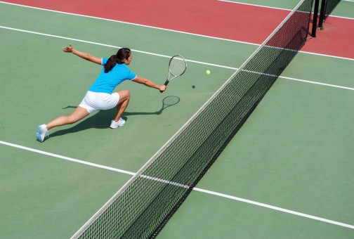 High angle view of young woman hitting a backhand volley on public tennis court.