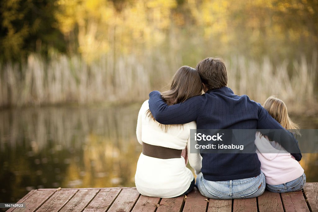 Family of Three Sitting on Deck Overlooking Pond in Autumn Color image of a dad, mom, and little girl sitting on a deck overlooking a pond, on a sunny, fall day. 20-29 Years Stock Photo