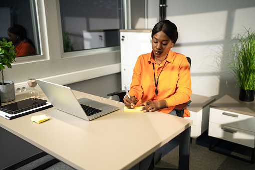 Beautiful African businesswoman taking notes while working in office at night