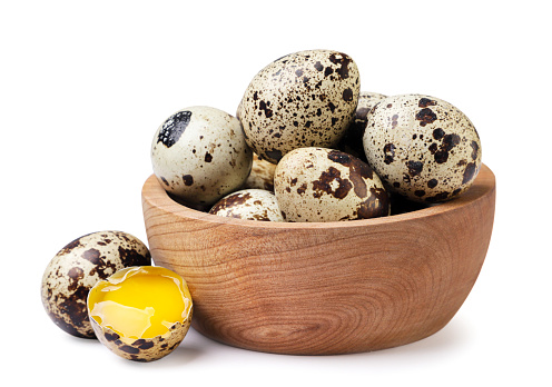 Quail eggs in a wooden plate and broken close-up on a white background. Isolated