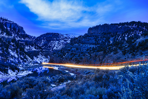 Night Highway Driving Time Exposure - Scenic Glenwood Canyon along Interstate 70 in Western Colorado with vehicles creating light trails and streaks during blue hour dusk. Night winter landscape along Colorado River with interstate and train tracks running through rugged canyon. Dotsero-Glenwood Springs, Colorado USA.