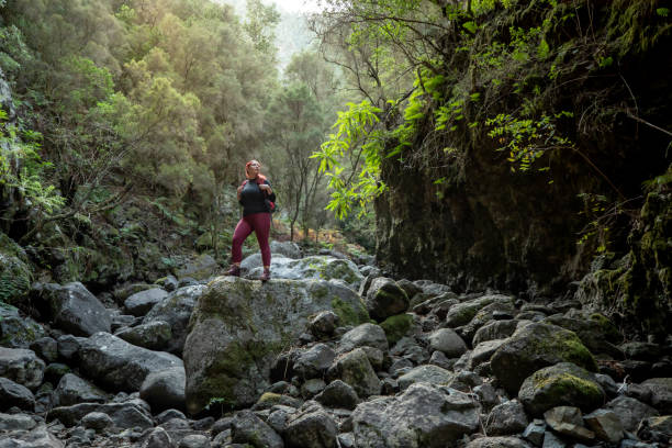 Woman standing still on top of a boulder contemplating her surroundings while doing a beautiful nature trail during her vacation.